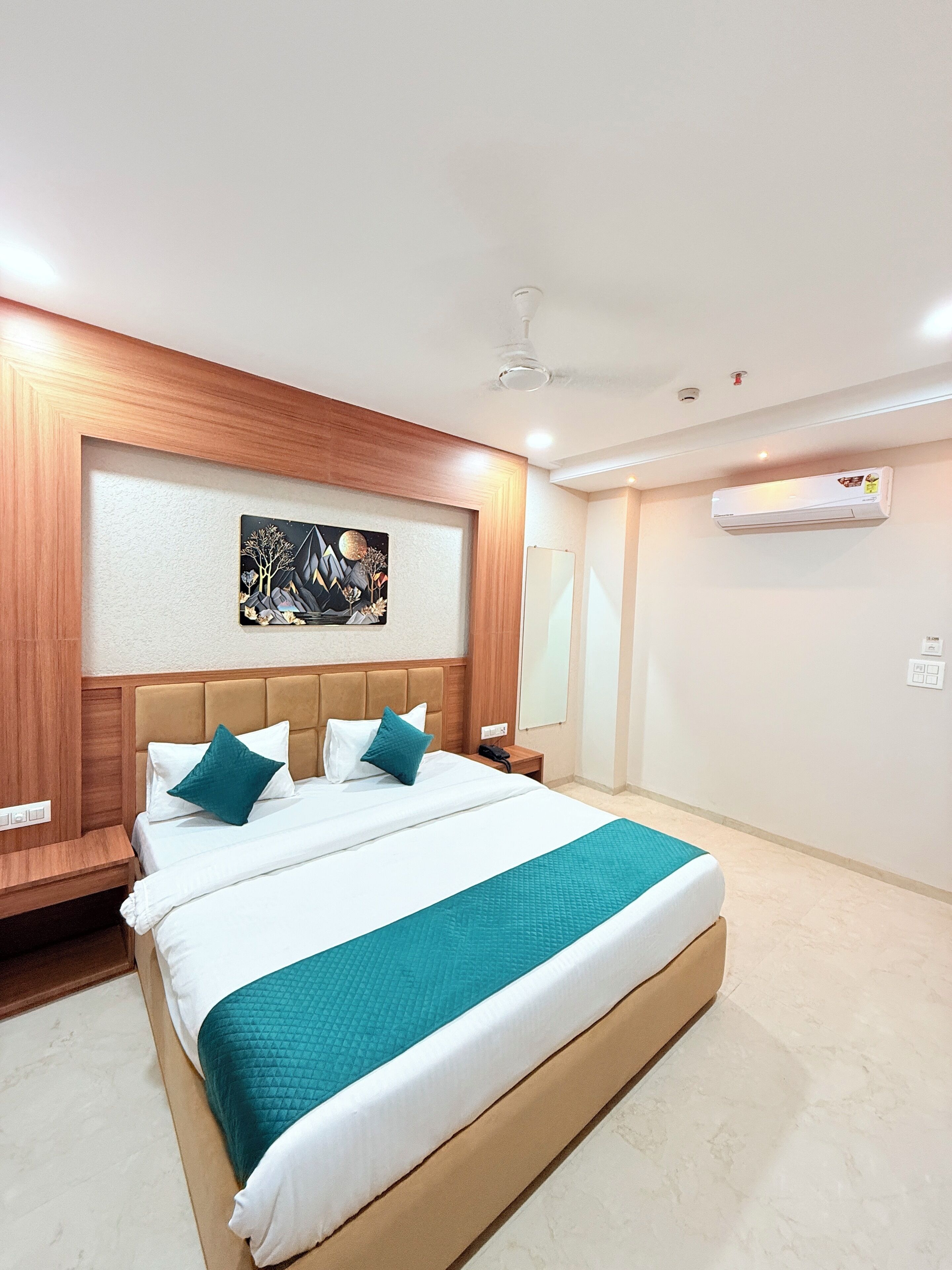 A modern hotel room with a large bed, wooden headboard, and a wall-mounted air conditioner.