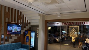 A hotel reception area with a modern design, including a reception desk, seating area, and a television displaying news. - Hotel Akaay (Ujjain)