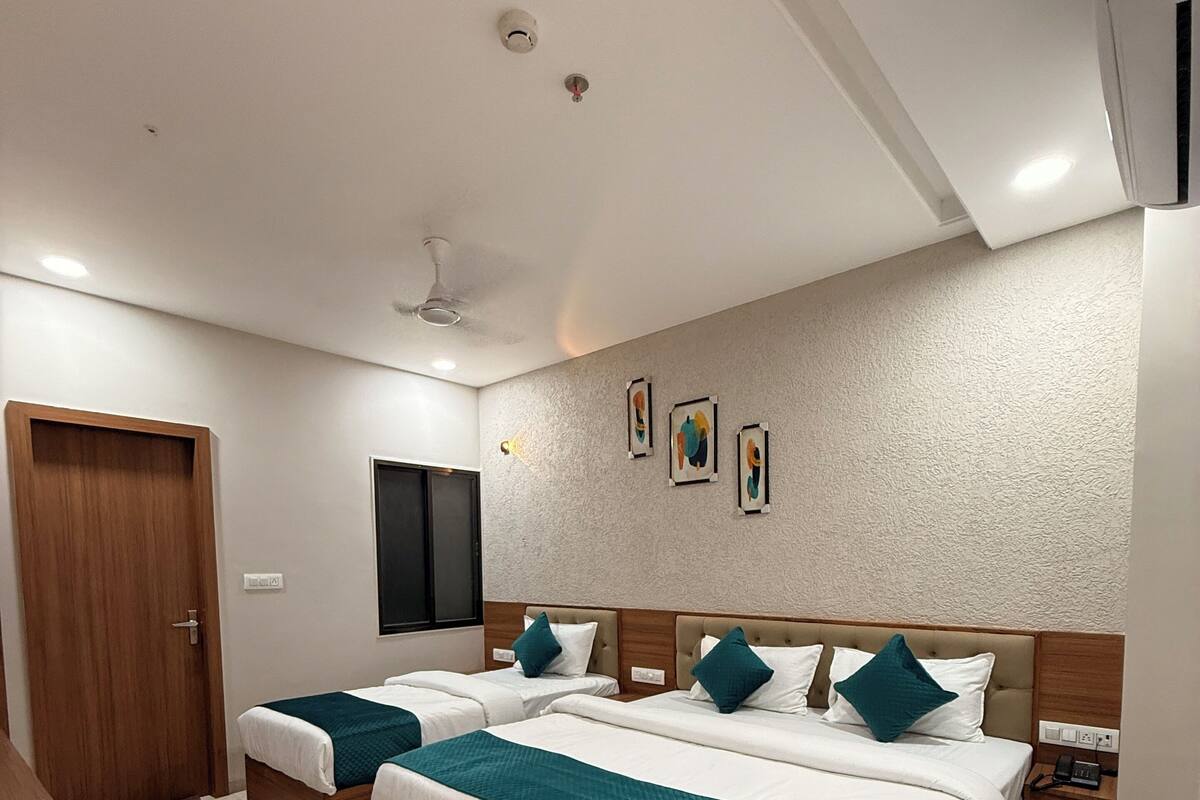 A hotel room with two beds, a wooden wardrobe, a ceiling fan, and artwork on the wall.