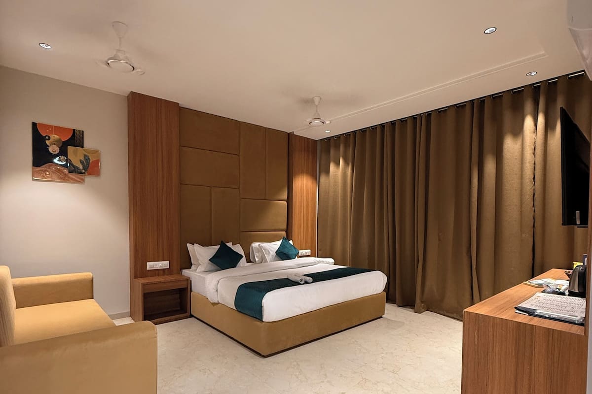 A modern hotel room with a large bed, a desk, a chair, and a painting on the wall.
