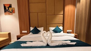A hotel room with a large bed, a headboard, a nightstand, a lamp, and a painting on the wall. - Hotel Akaay (Ujjain)