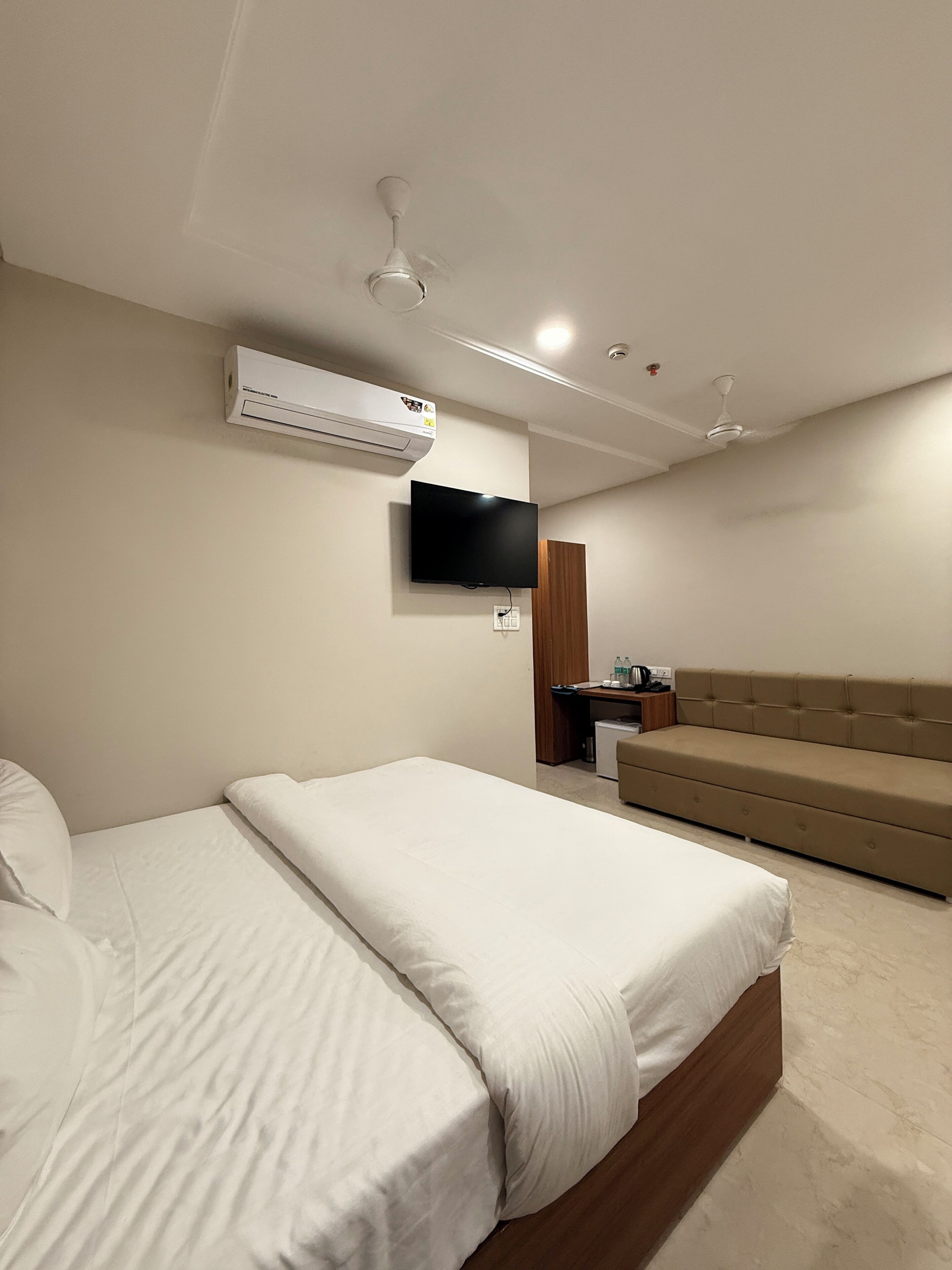 Una habitación de hotel moderna con una cama grande, un sofá, un televisor de pantalla plana, un equipo de aire acondicionado y un escritorio con una silla.