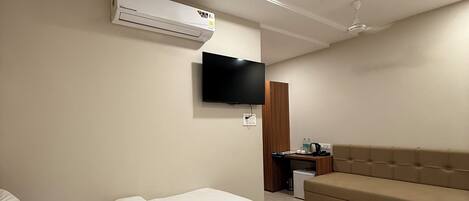 Una habitación de hotel moderna con una cama grande, un sofá, un televisor de pantalla plana, un equipo de aire acondicionado y un escritorio con una silla.