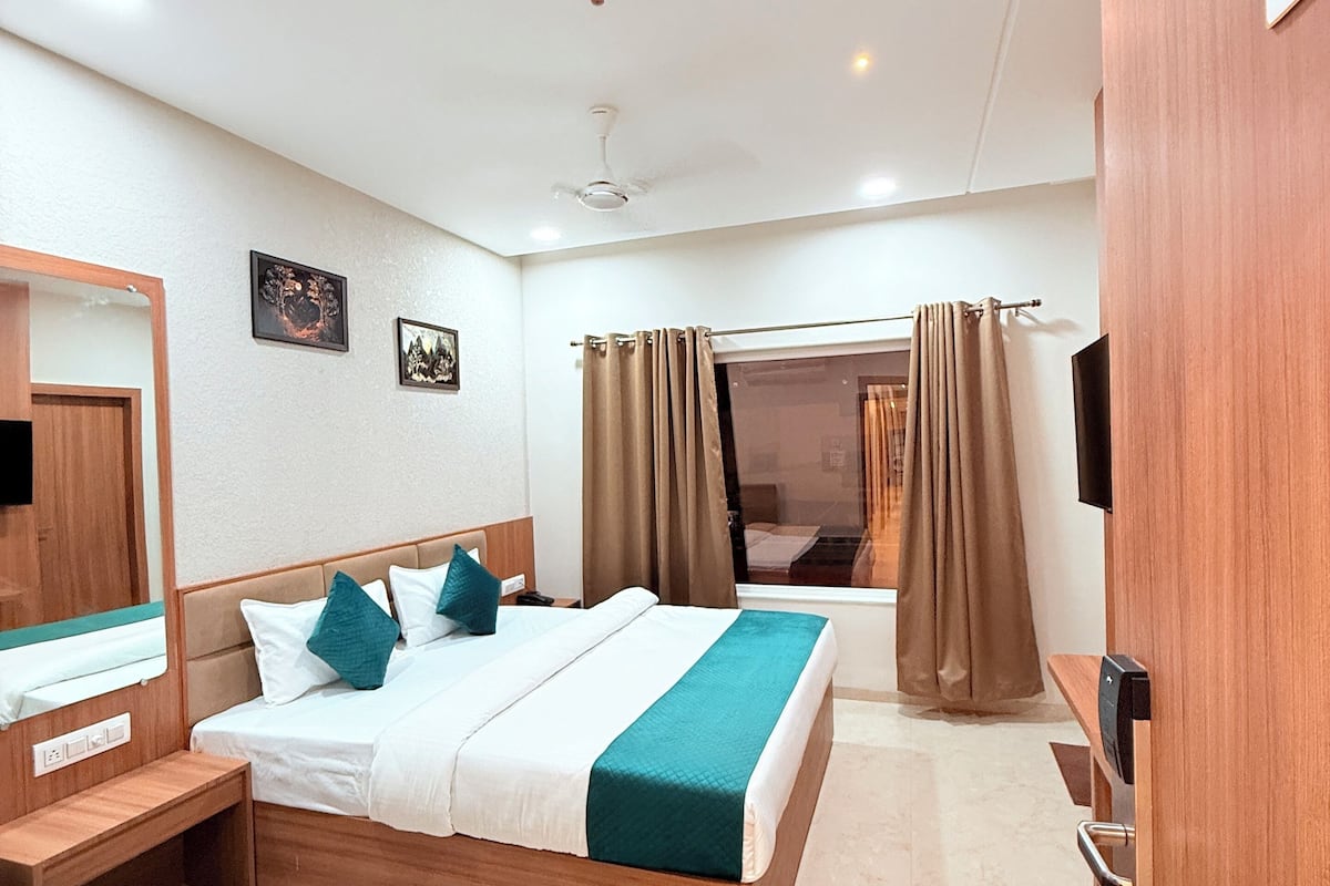 A hotel room with a bed, a desk, a mirror, a TV, and a wardrobe.