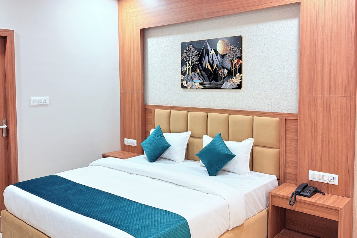 A modern hotel room with a large bed, a headboard with built-in lighting, a bedside table with a phone, and a wall-mounted artwork.