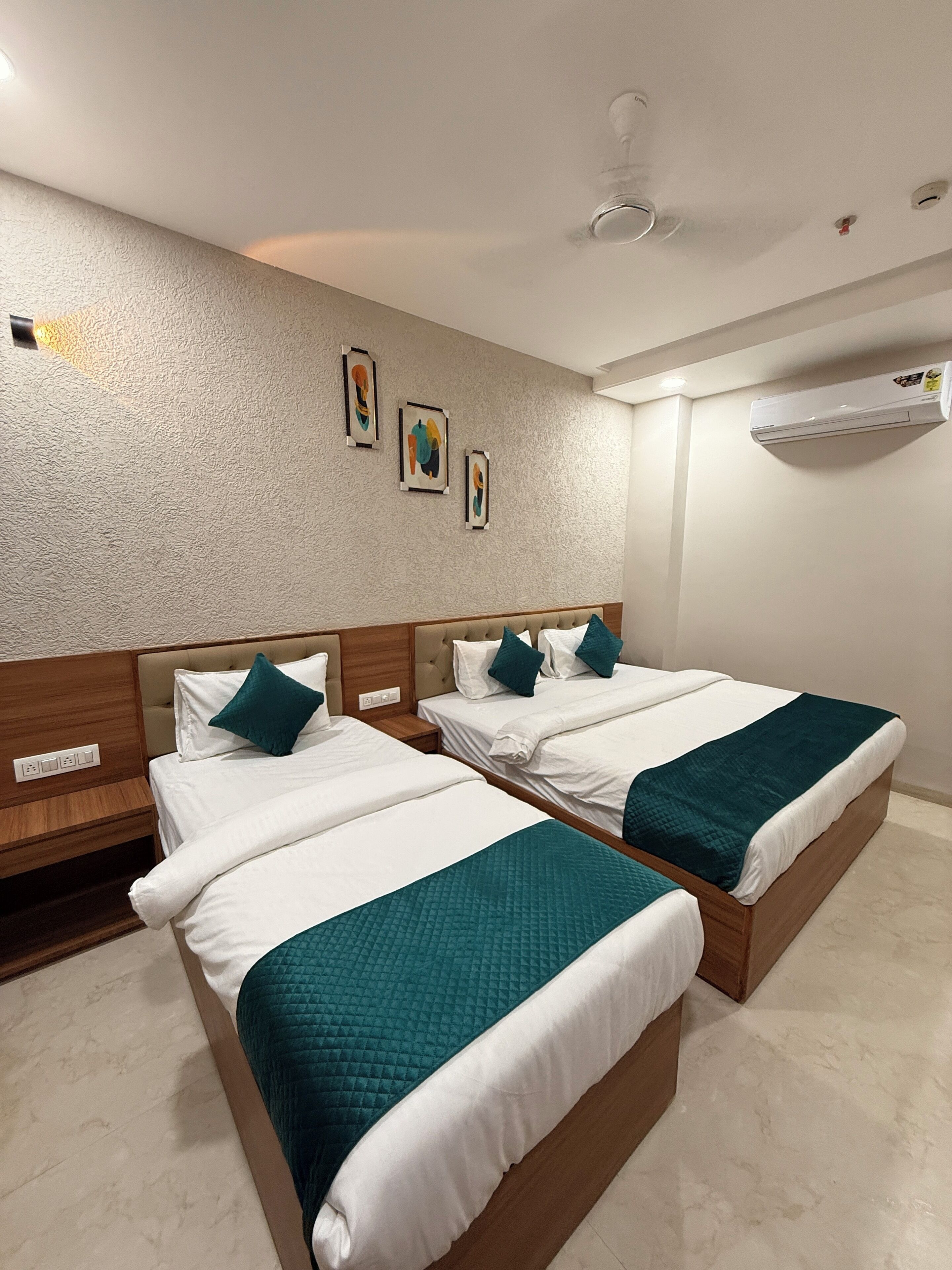 Habitación de hotel con dos camas, ventilador de techo, aire acondicionado y obras de arte en la pared.