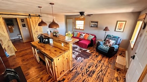 Un amplio salón con una barra de madera, un sofá rojo, un sillón azul y una alfombra de cuero de vaca.