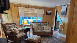 Una sala de estar acogedora con piso de madera, un sofá a cuadros, un sillón de madera y un reposapiés a juego.