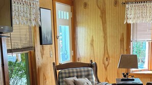 Una habitación acogedora con paneles de madera, un sillón a cuadros, un reposapiés a juego, una mesita con lámpara y un televisor en la pared.