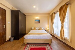 Une chambre d’hôtel avec un grand lit, une armoire, un tableau au mur et une fenêtre avec des rideaux.