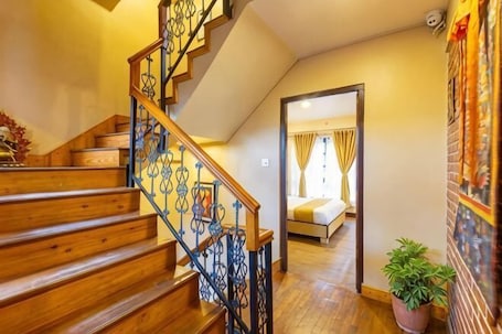 A wooden staircase with a metal railing leading to a bedroom with a bed and curtains.. Bhrikuti Stay