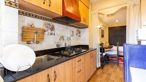 A compact kitchen with wooden cabinets, a black countertop, and a small dining area with a table and chairs. - Bhrikuti Stay (Lalitpur)
