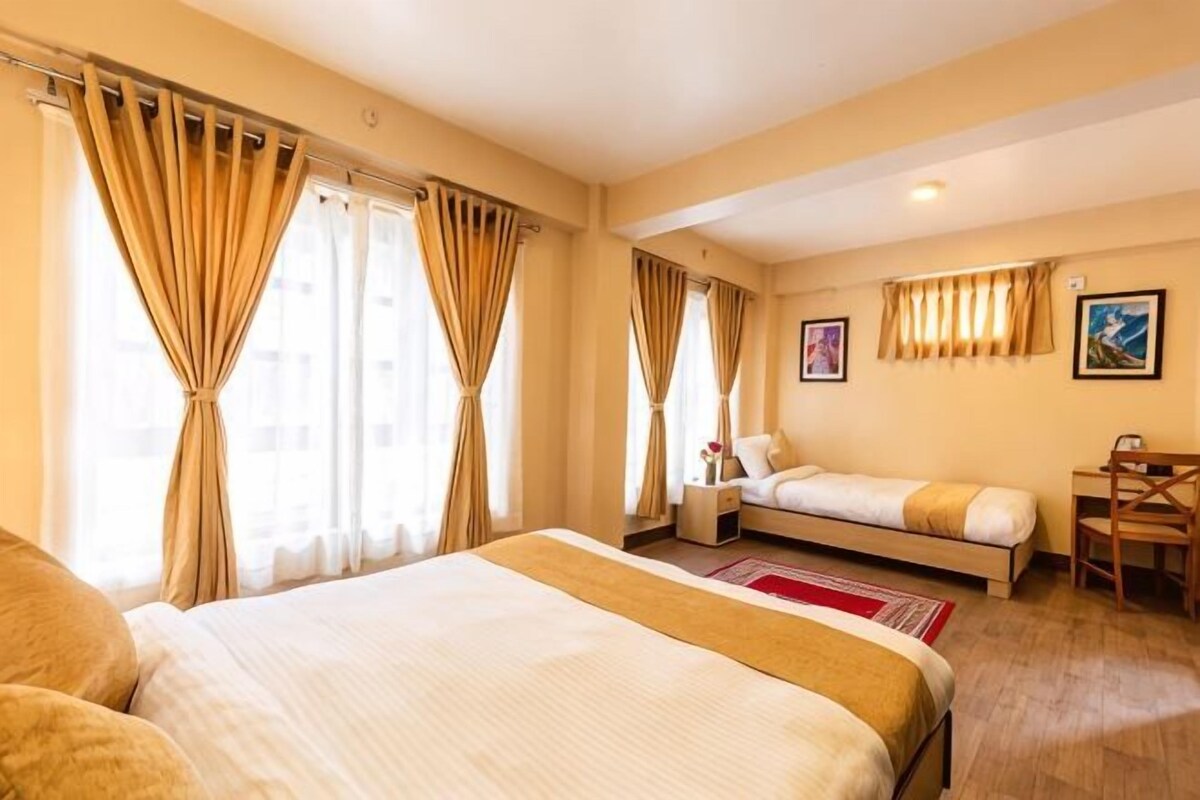 A hotel room with a large bed, a smaller bed, a desk, and a chair.
