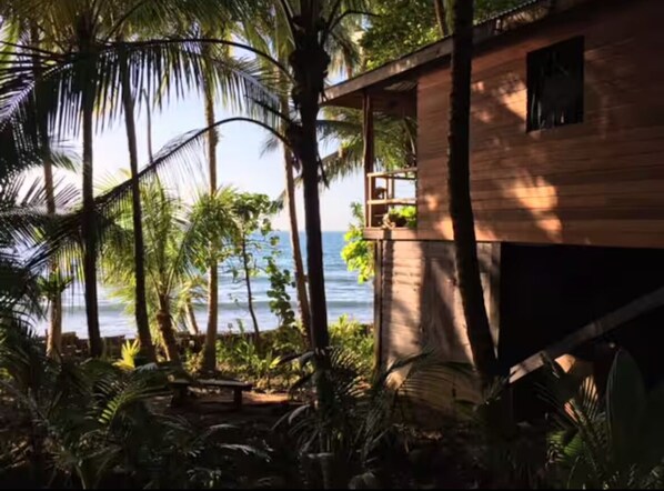 Un edificio de madera con balcón que da a una playa y al océano.
