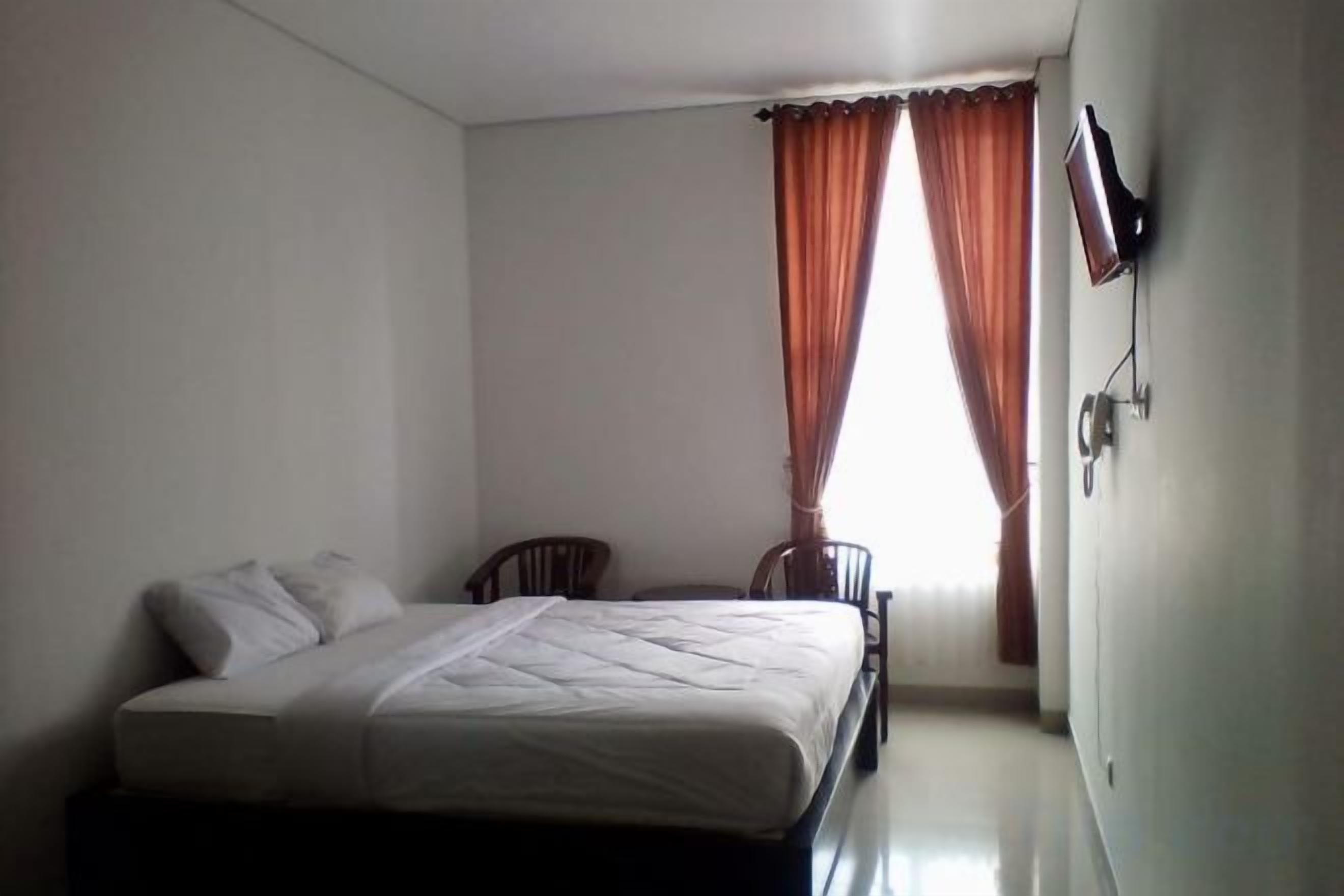 Un dormitorio con una cama, dos sillas, un televisor y una ventana con cortinas.