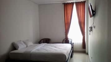 Un dormitorio con una cama, dos sillas, un televisor y una ventana con cortinas.