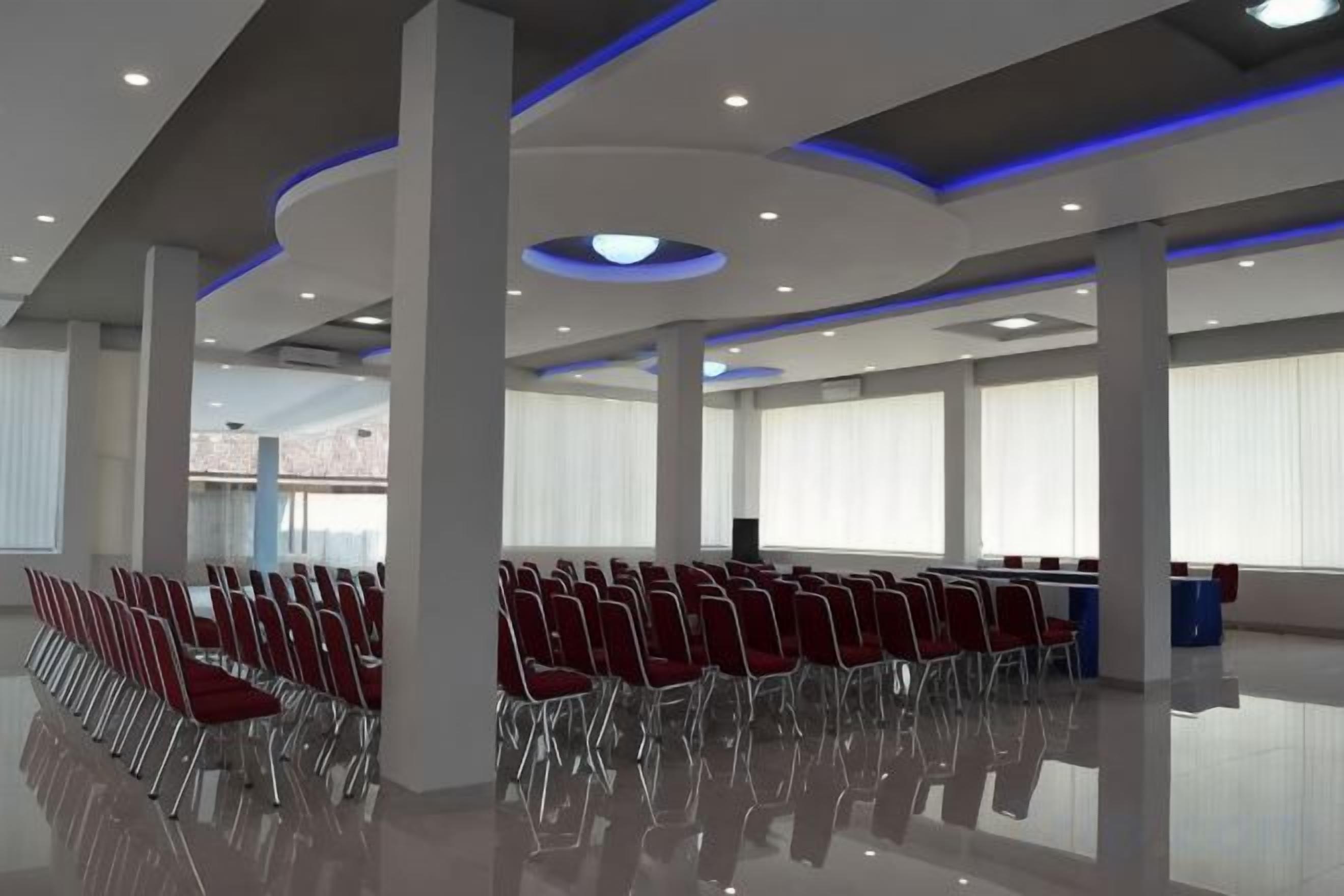A spacious hall with rows of chairs, large windows, and a modern ceiling design.