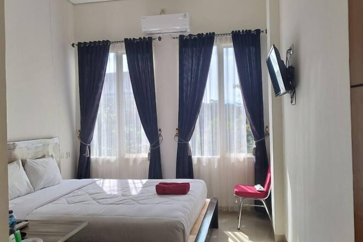 Una habitación de hotel con una cama, una silla y un televisor montado en la pared.