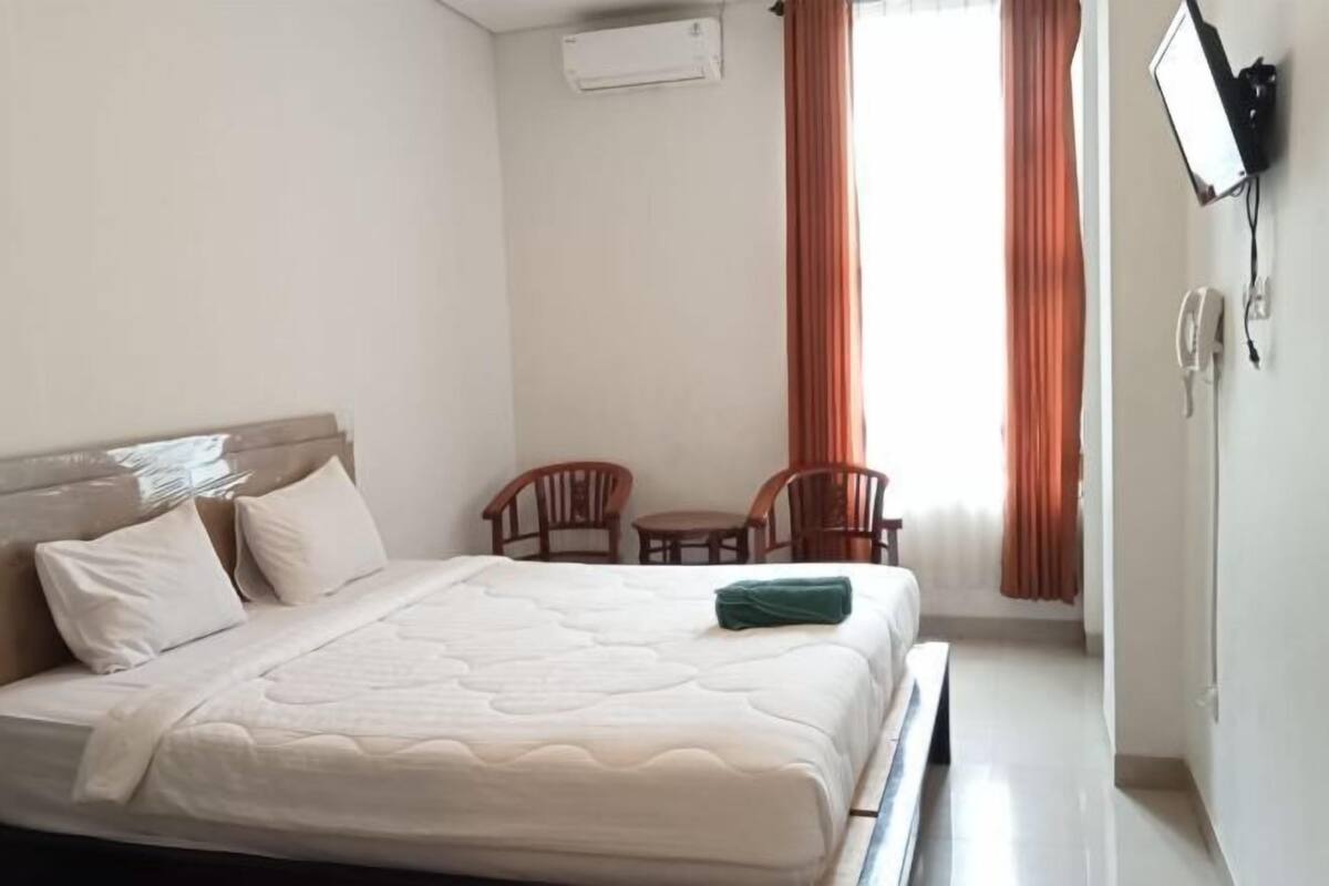 Habitación de hotel con cama, escritorio, dos sillas, aire acondicionado y televisor en la pared.