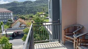 A balcony with a railing, a wooden chair, and a view of a town with buildings and greenery.