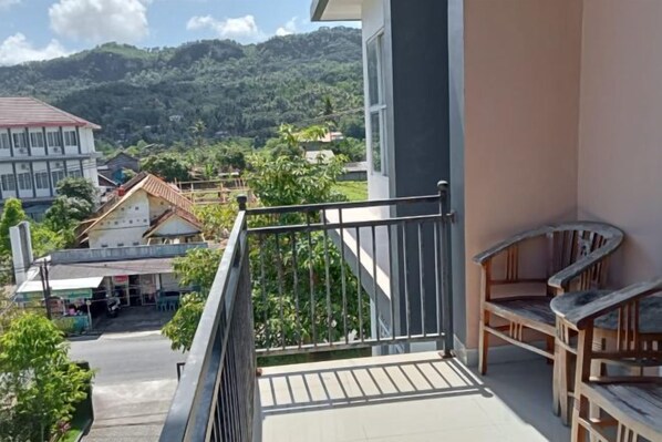 A balcony with a railing, a wooden chair, and a view of a town with buildings and greenery. - Hotel Grand Bromo Pacitan (Pacitan)