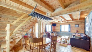 Interior de una cabaña de madera con comedor, sofá y escalera.