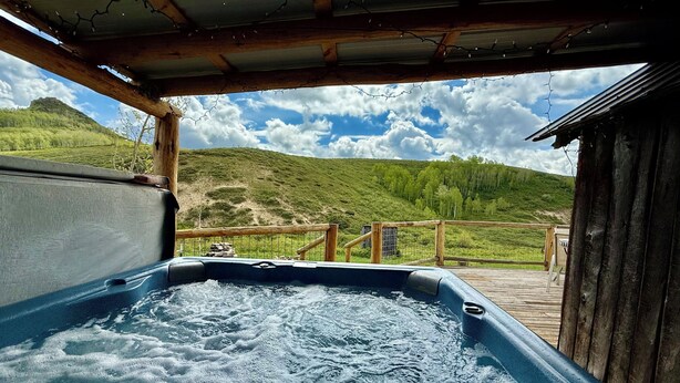 Un jacuzzi con cubierta de madera y vista a una ladera verde.