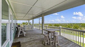 A covered porch with wooden flooring, a table, and two chairs. - Near Marina~Near Beach~Chef Kitchen~Games~Balcony (Bolivar Peninsula)