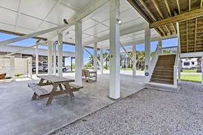Un área de patio techada al aire libre con mesas de picnic, una escalera y vistas a vehículos estacionados y casas al fondo.