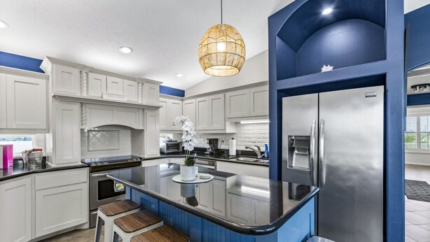A modern kitchen with white cabinets, a central island with stools, a stainless steel refrigerator, and a hanging light fixture. - Near Marina~Near Beach~Chef Kitchen~Games~Balcony (Bolivar Peninsula)