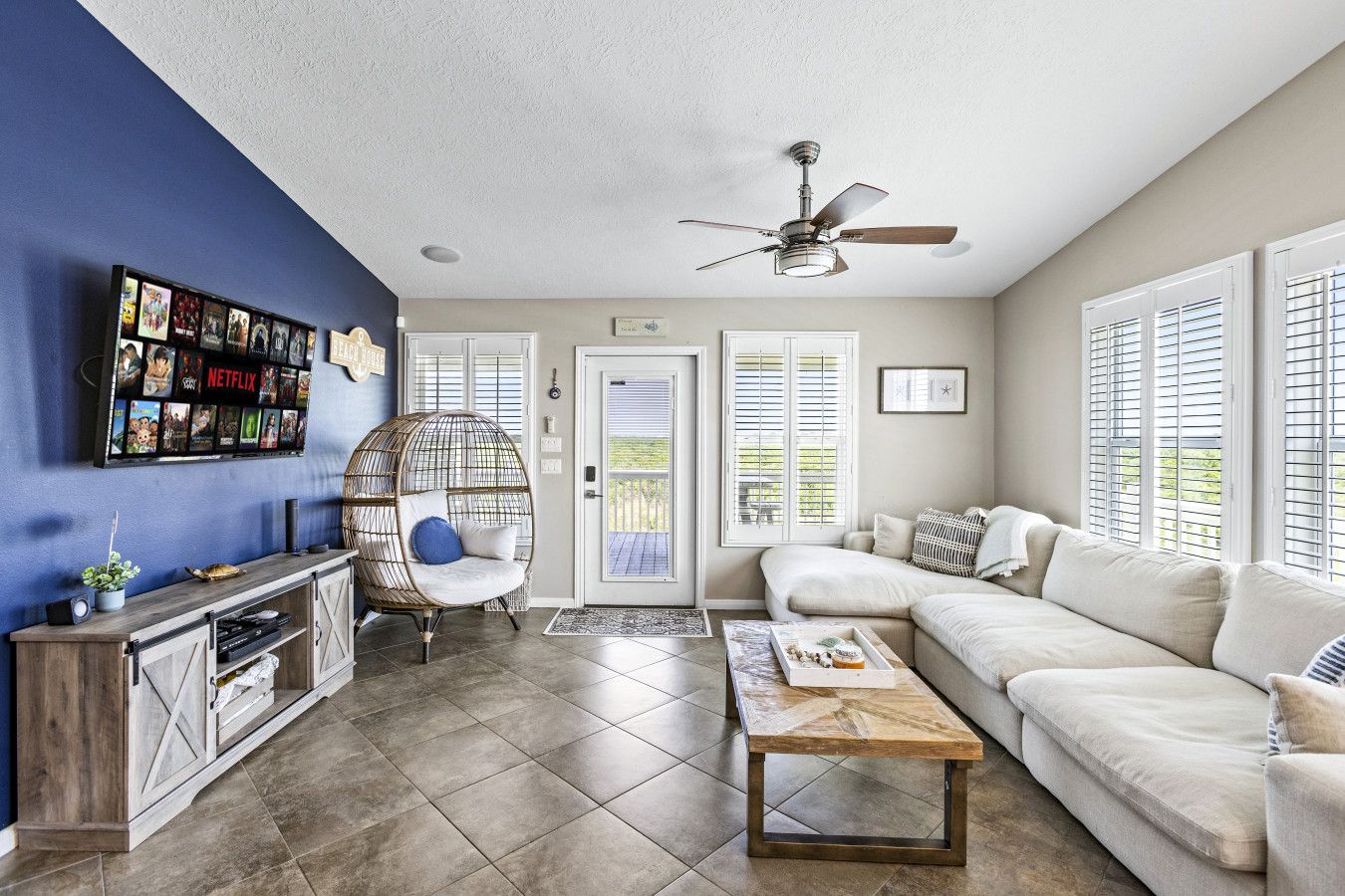 A living room with a blue accent wall, a ceiling fan, a white sofa, a wooden coffee table, and a decorative chair.