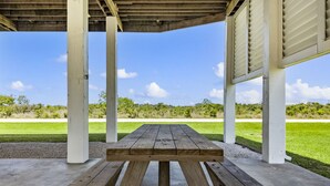 A wooden picnic table under a covered area with a view of a grassy field and trees. - Near Marina~Near Beach~Chef Kitchen~Games~Balcony (Bolivar Peninsula)