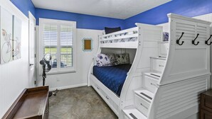 A bunk bed room with white walls, a blue accent wall, a window with blinds, a fan, and a bicycle-themed artwork. - Near Marina~Near Beach~Chef Kitchen~Games~Balcony (Bolivar Peninsula)