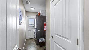 Un couloir avec une porte blanche sur la droite, une fenêtre sur la gauche et un extincteur fixé au mur.
