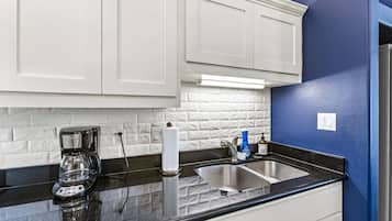 A kitchen with white cabinets, a black countertop, a coffee maker, a paper towel holder, and a sink with a faucet.