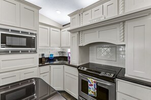 Una cocina con armarios blancos, microondas, estufa y salpicadero de azulejos.