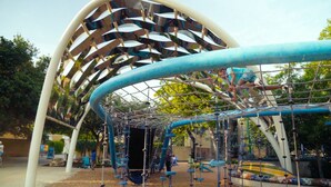 An outdoor playground with a netted climbing structure and a large, curved white arch.
