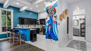 A modern kitchen with dark cabinets, a blue accent wall, and a mural of a colorful figure.