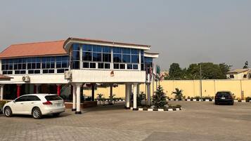 A building with a red roof and large windows, a white car parked in front, and several flags.