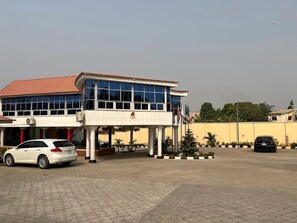A building with a red roof and large windows, a white car parked in front, and several flags. - Marchforte-Courtyard Hotel  (Ibadan)