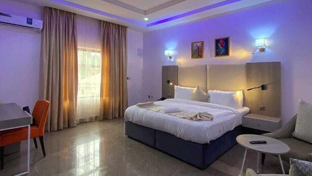 A modern hotel room with a large bed, bedside tables, a desk, and a chair. - Marchforte-Courtyard Hotel  (Ibadan)