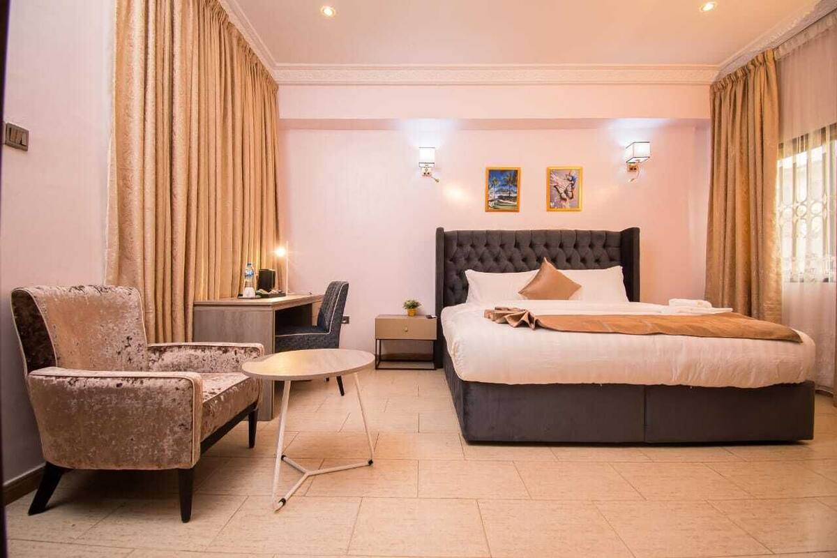 Hotelkamer met een groot bed, een stoel, een klein tafeltje en twee wandlampen.