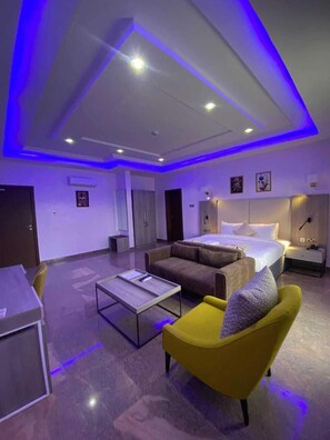 A modern hotel room with a bed, a sofa, a yellow armchair, a small table, and a desk. - Marchforte-Courtyard Hotel  (Ibadan)