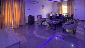 A modern living room with a sofa, armchairs, and a coffee table. There is a flat-screen TV mounted on the wall. - Marchforte-Courtyard Hotel  (Ibadan)
