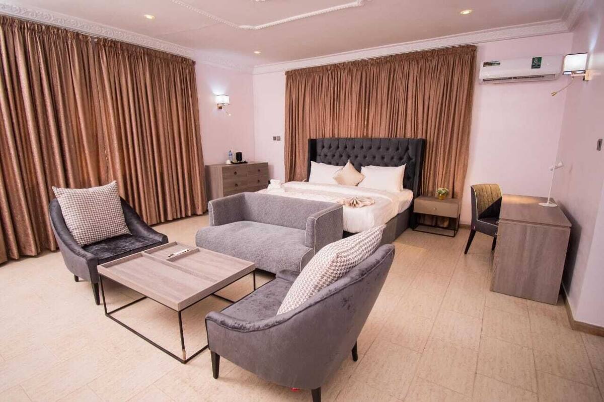 Een moderne hotelkamer met een groot bed, twee fauteuils, een bank, een tafeltje en een bureau.