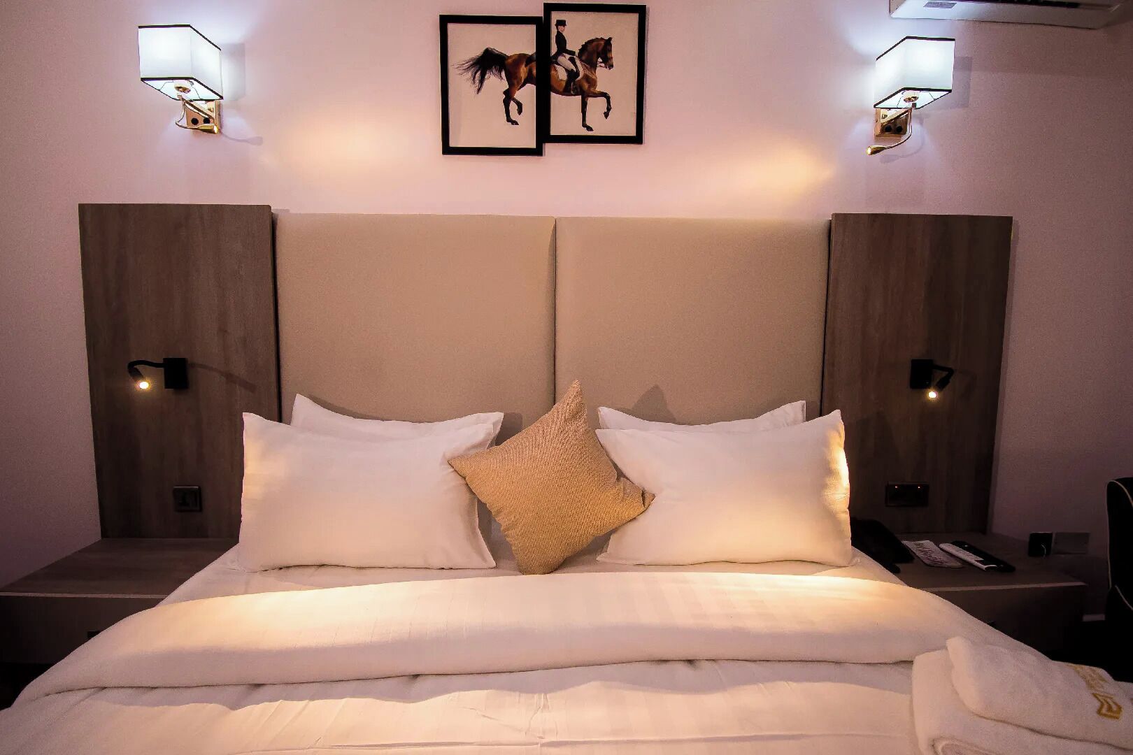 Una habitación de hotel con una cama grande, dos lámparas de pared y dos cuadros con caballos.