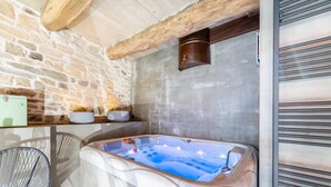 Een wellnessruimte met een stenen muur, een houten balk en een jacuzzi, plus een stoel.