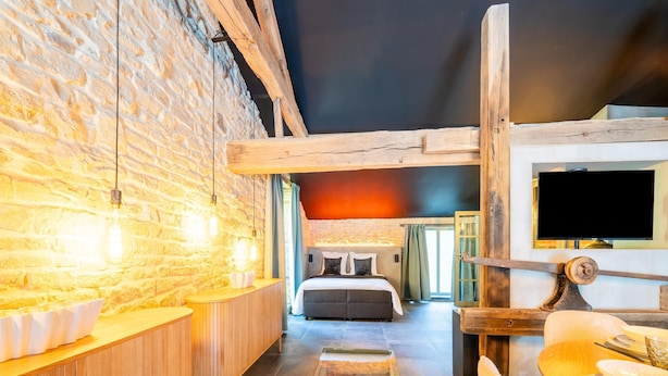 Een rustieke hotelkamer met zichtbare bakstenen muren, een houten receptiebalie, een bed met hoofdeinde en een aan de muur bevestigde televisie.