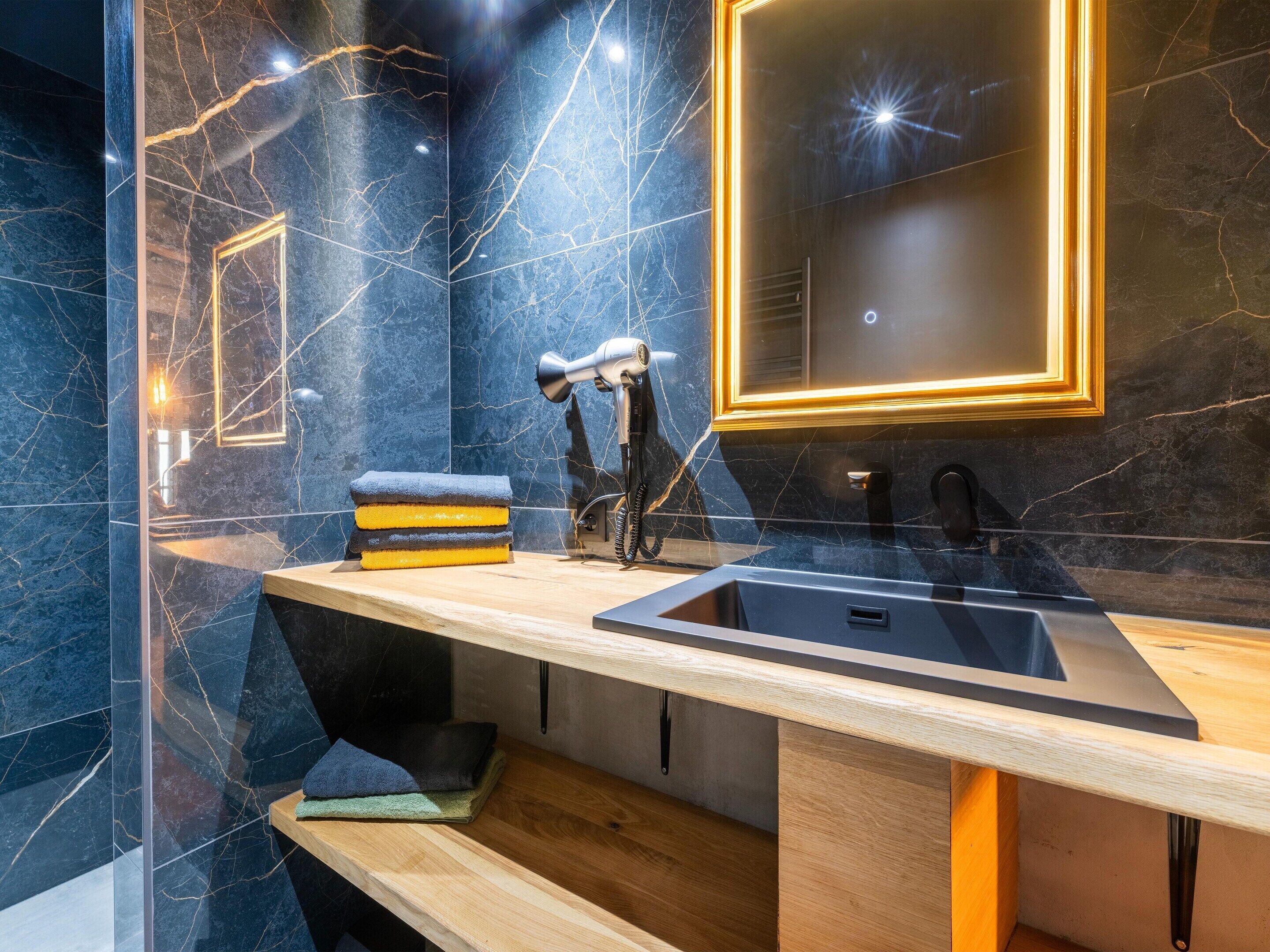 Un baño moderno con salpicadero de mármol, tocador de madera, lavamanos negro y un secador de pelo.