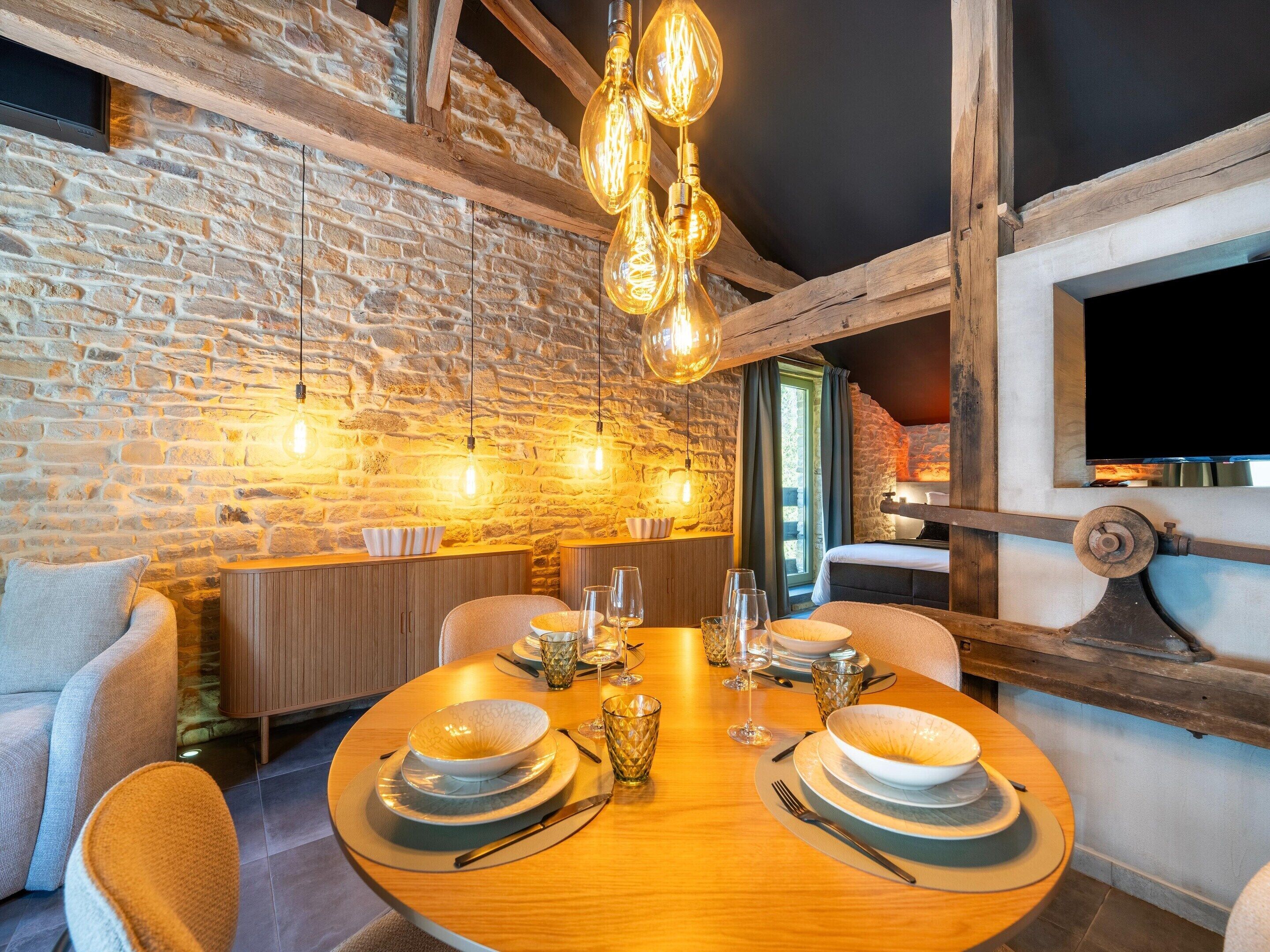 A dining area with a stone wall, wooden beams, and hanging light fixtures.